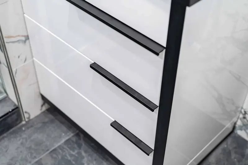 White vanity drawers with long black bar pulls beside the marble-look wainscot