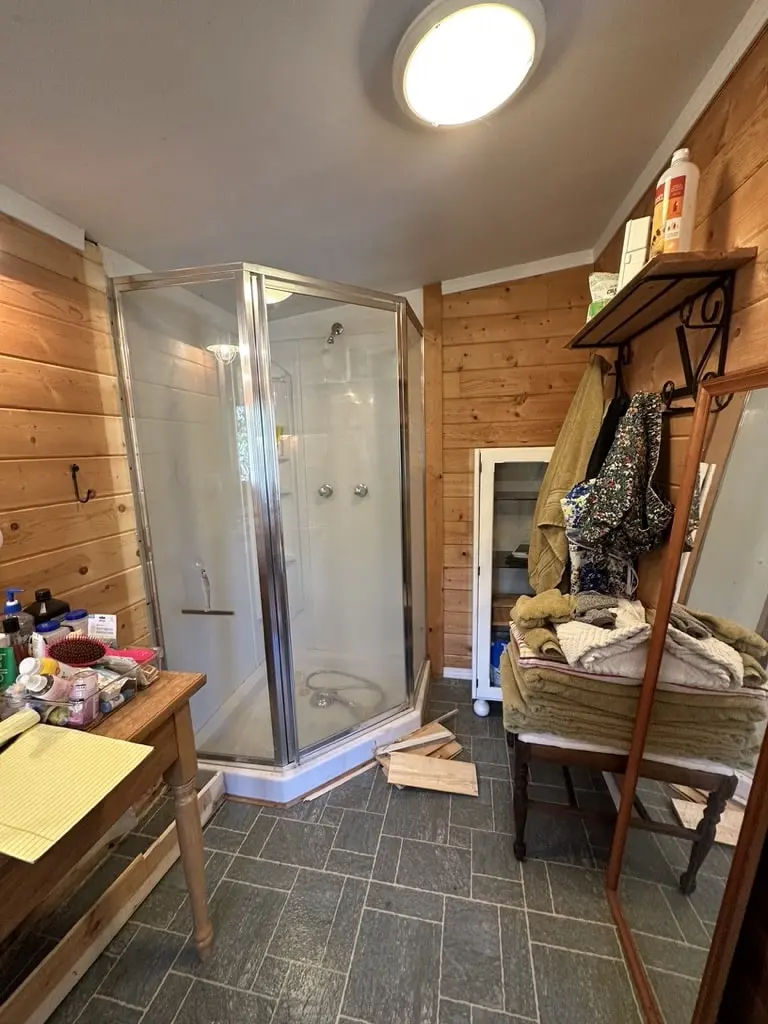 Knotty pine bathroom before the remodel with a framed corner shower stall and a slate-look tile floor