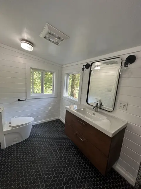 Remodeled bathroom with white shiplap walls, a floating wood vanity, a black framed mirror and a black hexagon tile floor