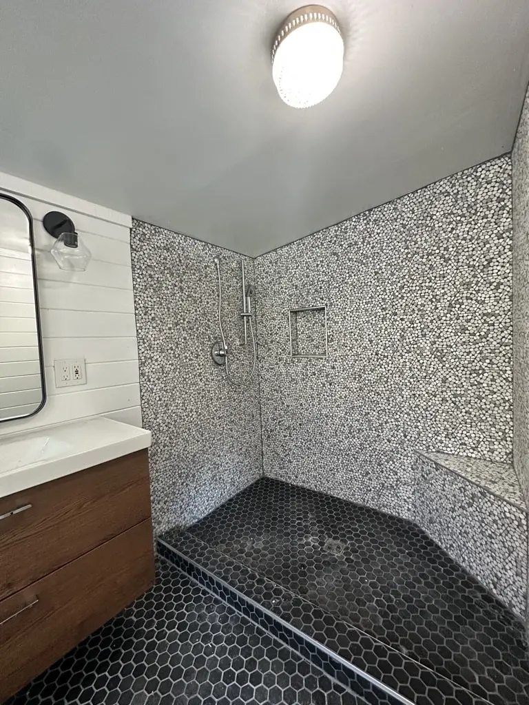 Shower corner bench and niche in mosaic tile beside the vanity and a black framed mirror