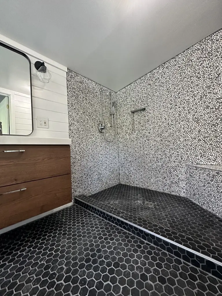 View from the vanity into the large walk-in shower with mosaic walls and a black tile floor