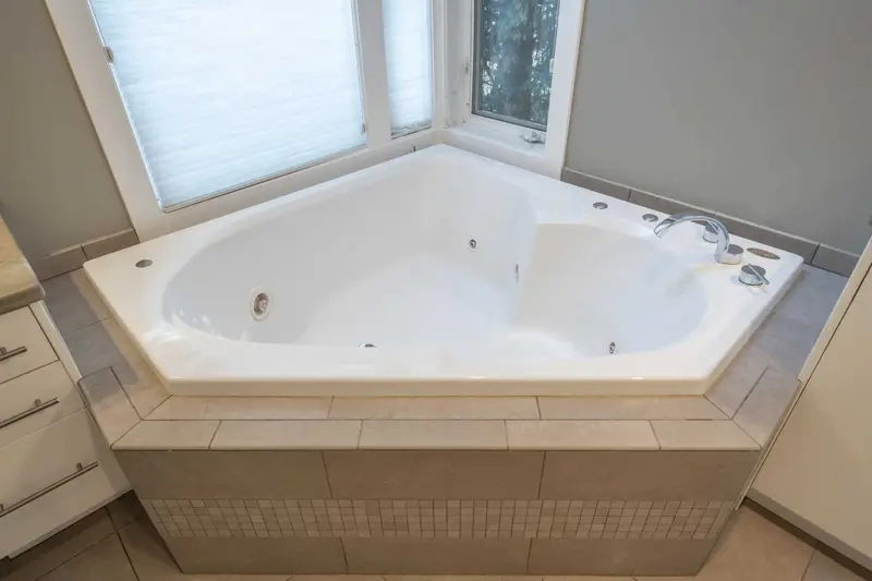 Large corner jetted tub with a tiled deck under the windows