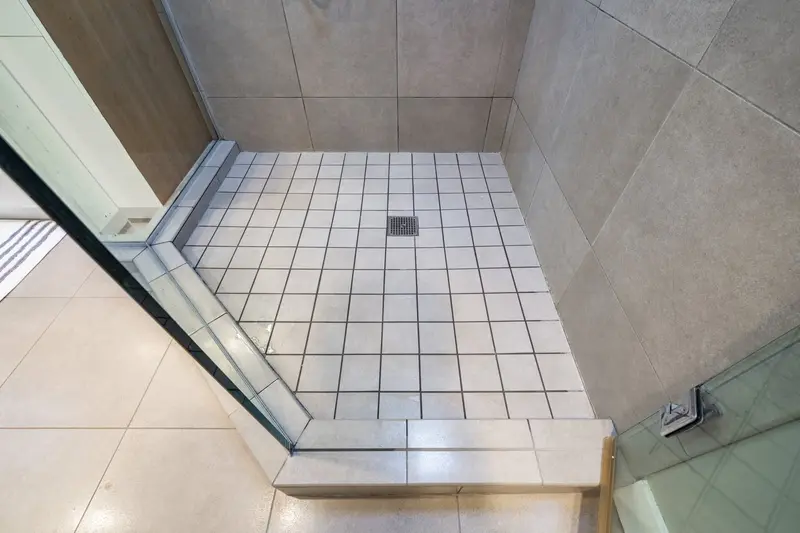 Old shower floor of small square tile with dark grout and a center drain