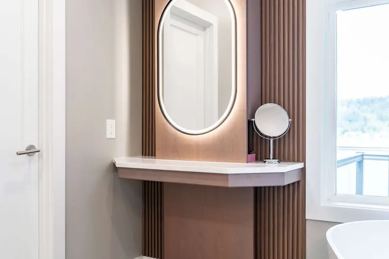 Sit-down vanity with an oval lit mirror and a wood slat panel beside a window