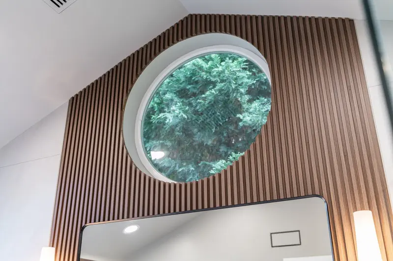 Round window framed by vertical wood slats under a sloped ceiling