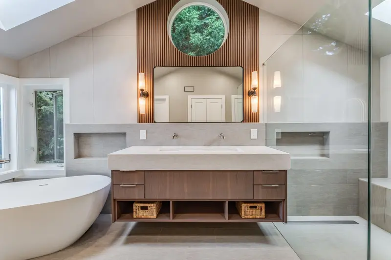 Floating vanity with a trough sink, wall sconces and a round window set in a wood slat wall