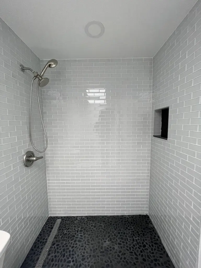 Walk-in shower with white glass subway tile walls, a recessed niche and a black pebble tile floor