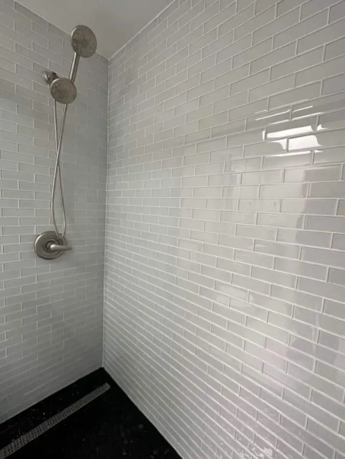Side wall of the shower in white glass subway tile with a handheld shower and valve
