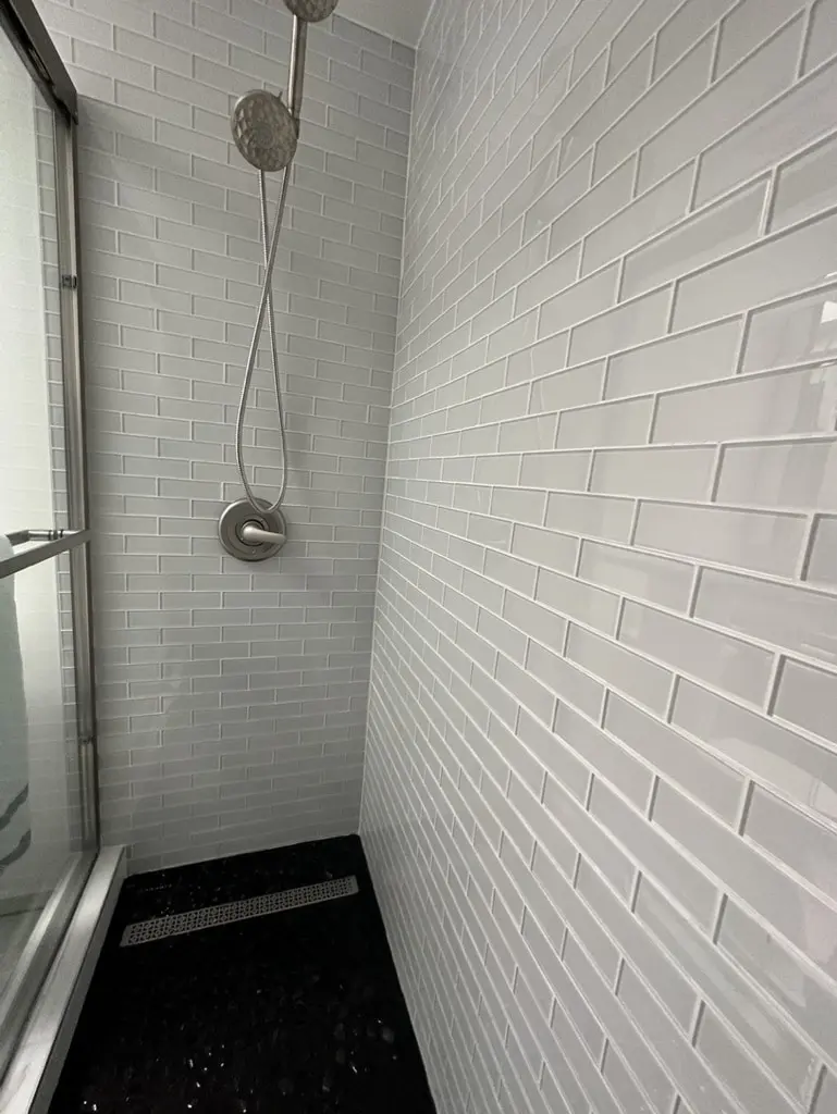 Shower wall with a handheld shower on a slide bar and a linear drain in the pebble floor
