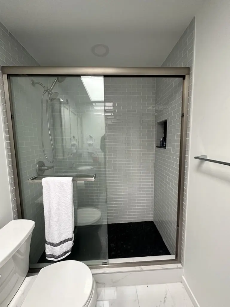 Sliding framed glass shower door in front of white subway tile and a black pebble floor