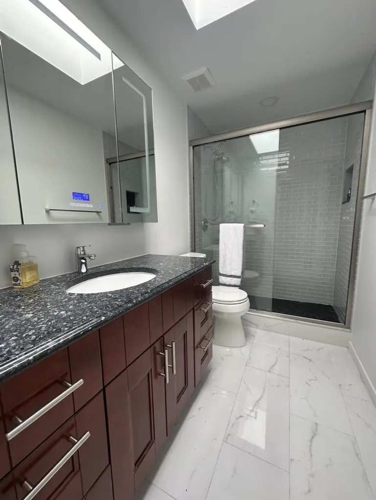 Long narrow bathroom with a dark wood vanity and dark stone top leading to a glass-enclosed subway tile shower