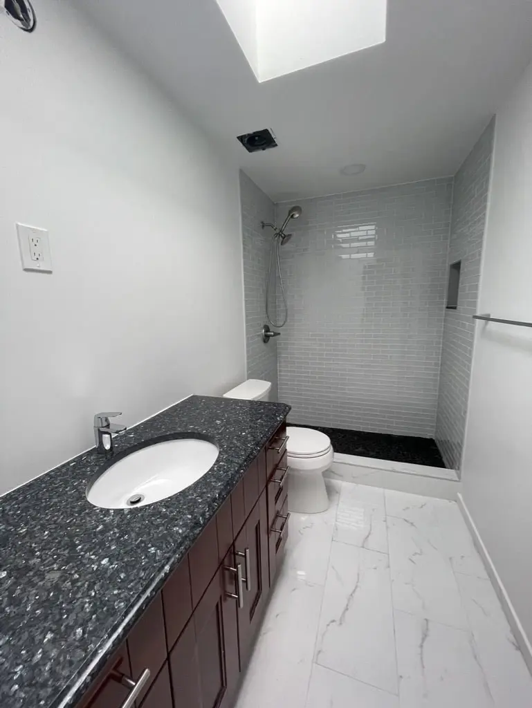 Dark stone vanity top with an undermount sink and the shower at the end of the room