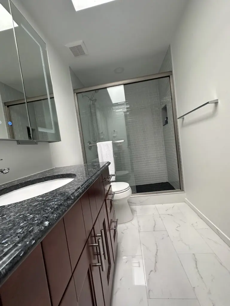 Bathroom with a skylight above a lit mirror cabinet, dark wood vanity and marble-look floor tile