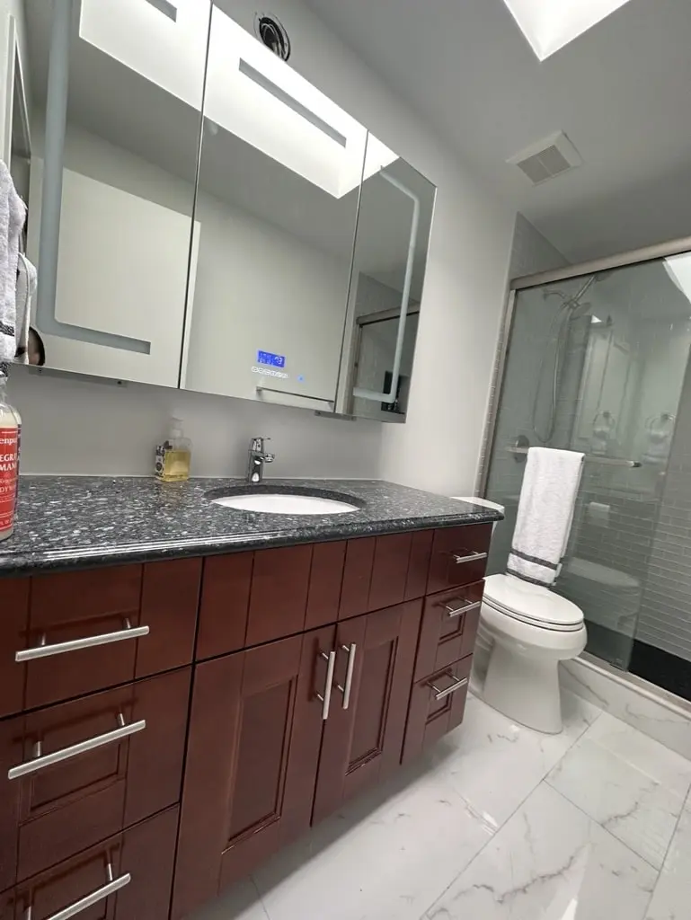 Dark wood shaker vanity with chrome pulls under a mirrored medicine cabinet