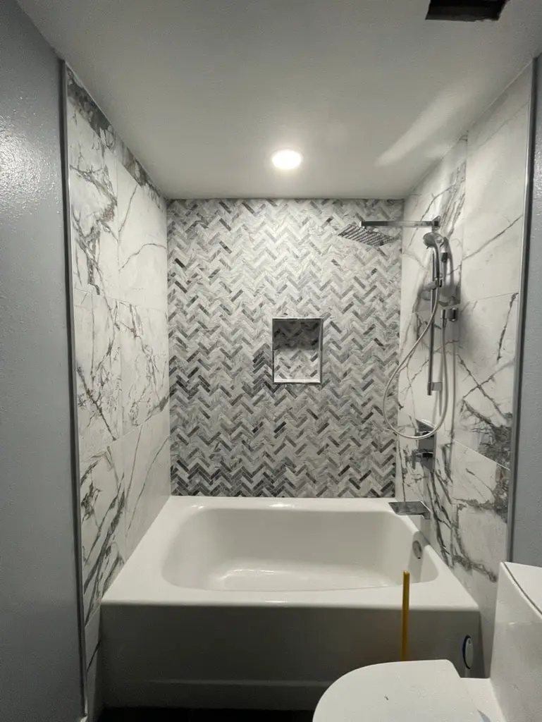 Alcove tub with a gray chevron mosaic back wall, a niche and white marble-look side walls