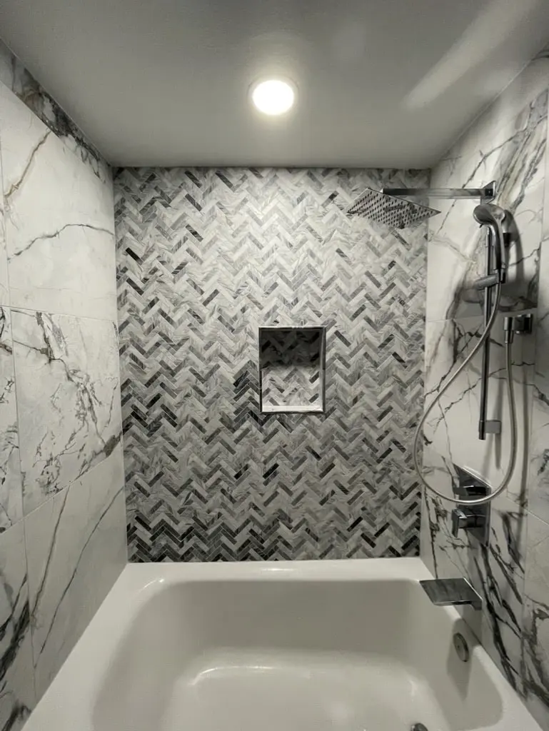 Chevron mosaic tub wall with a recessed niche, a square rain head and a handheld shower on a bar