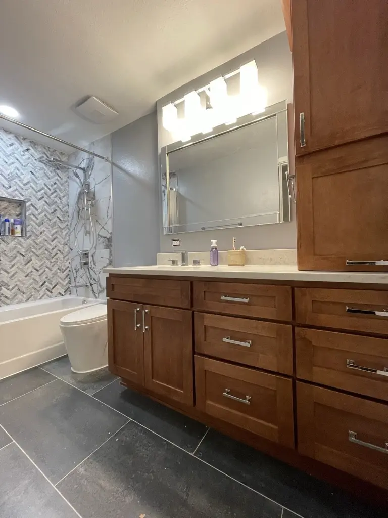 Hall bathroom with a light wood shaker vanity, light counter, three-light fixture and a tub with chevron mosaic tile