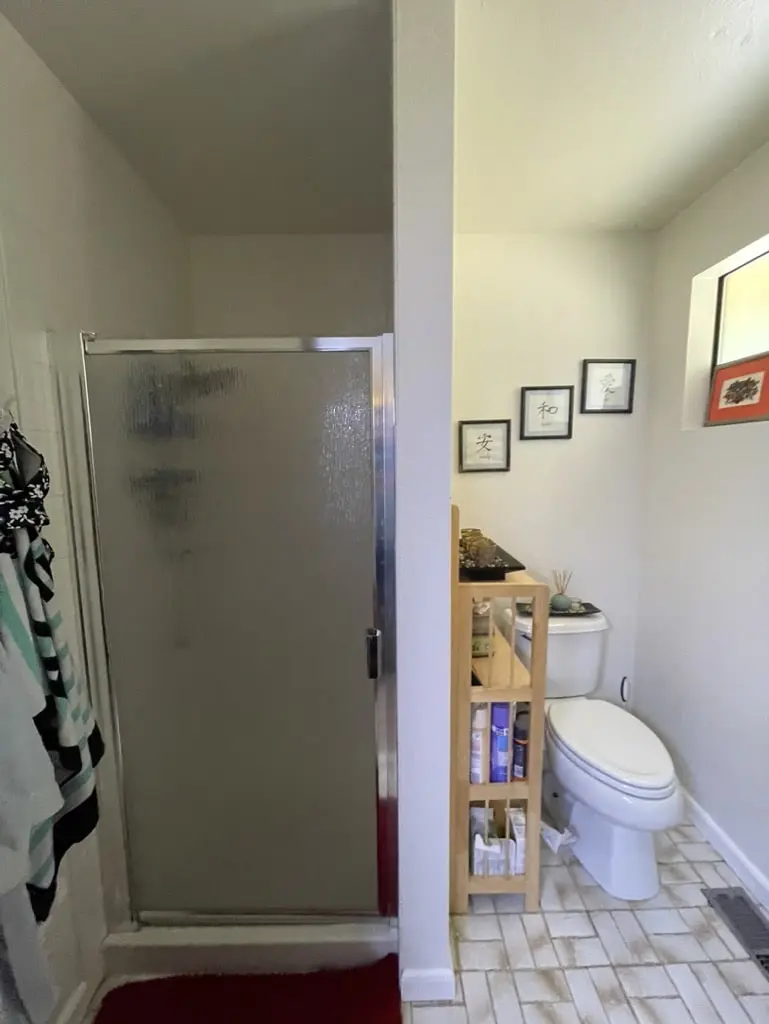 Old shower stall with a frosted glass door beside a toilet on a patterned tile floor
