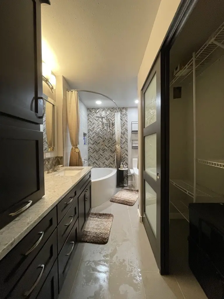 Primary bathroom with a long dark shaker vanity, sliding closet doors and a corner tub at the far end
