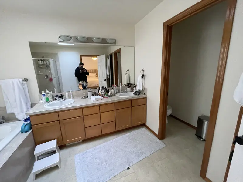 Oak double vanity with a long mirror and a globe light bar beside the open toilet room door