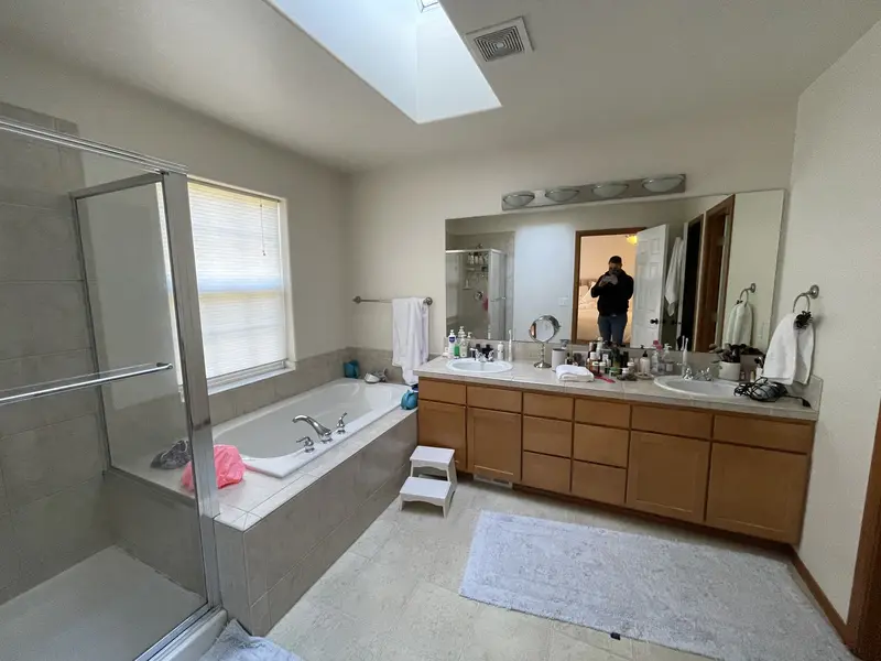 Bathroom before the remodel with a tiled tub deck under a window, a framed shower and an oak double vanity