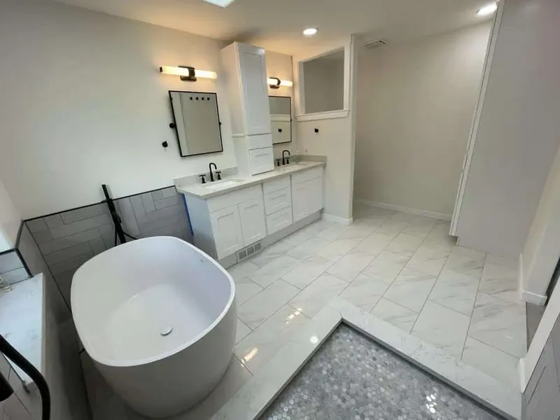 Freestanding white tub beside a black floor-mounted filler, with a pebble tile inset in the white floor