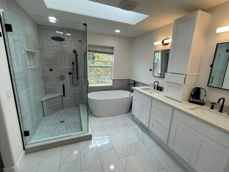Remodeled bathroom with a frameless glass shower, a freestanding tub under the window and a long white double vanity