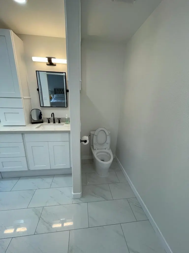 Toilet in an alcove beside the end of the white vanity, with marble-look floor tile
