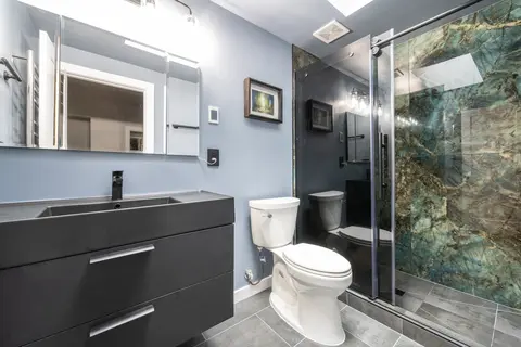 Black vanity and toilet beside the glass shower door, with the stone-look panels showing through