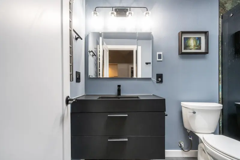 Floating black vanity with an integrated sink under a mirror cabinet and a four-light bar on a blue wall
