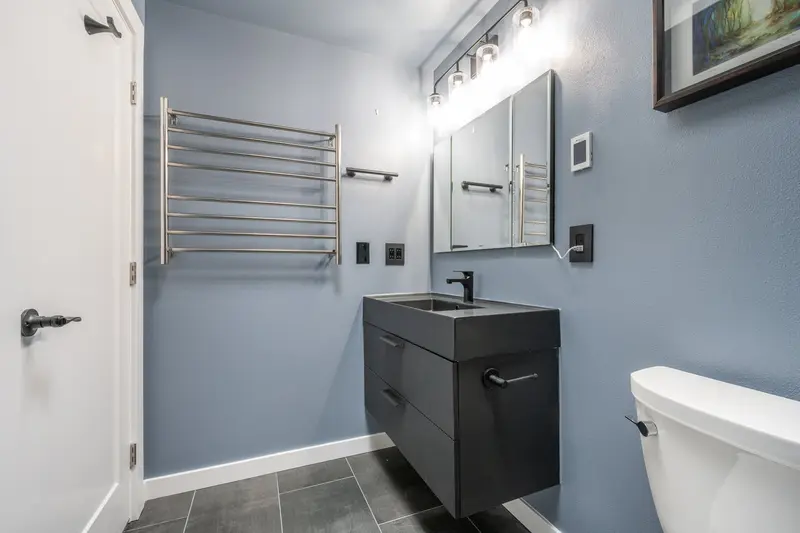 Stainless heated towel rack on a blue wall beside a floating black vanity and the bathroom door