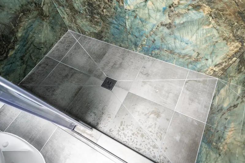 Gray shower floor tile sloping to a square drain, with the stone-look wall panels along two sides