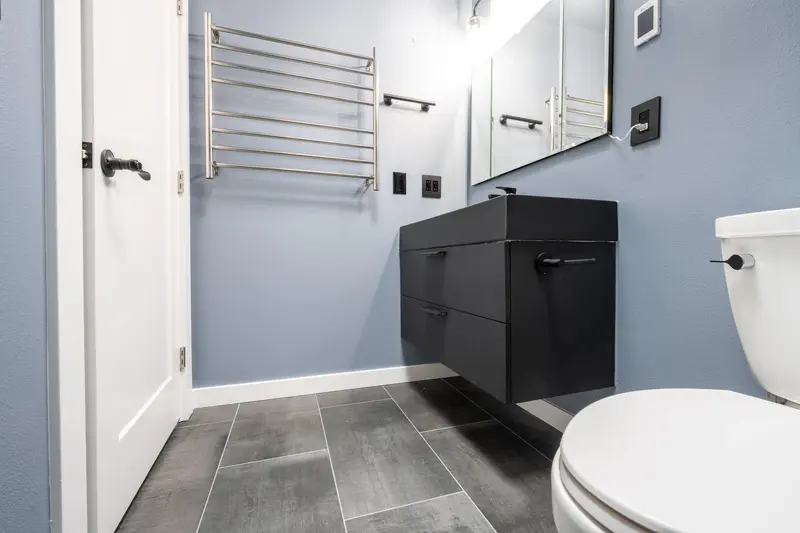 Heated towel rack, floating vanity and toilet seen from the doorway over a gray tile floor