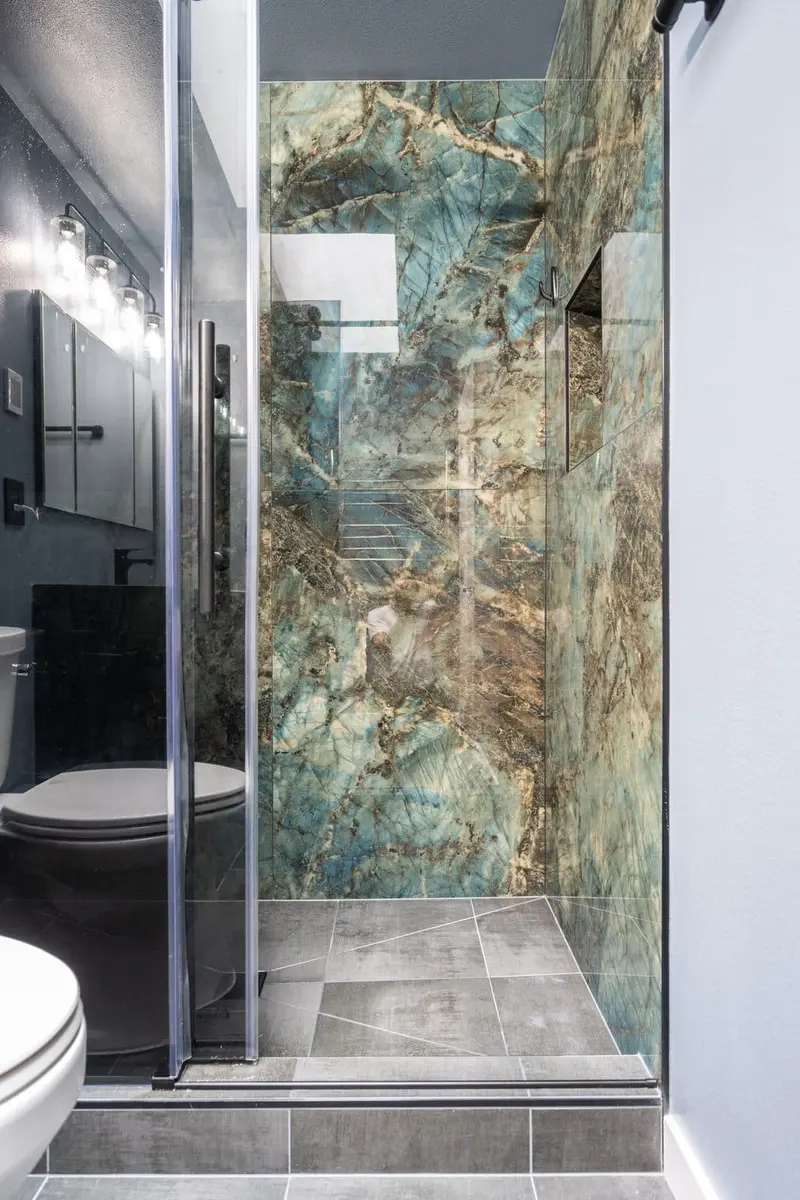Walk-in shower seen through its open glass door, with a skylight above and gray tile on the floor