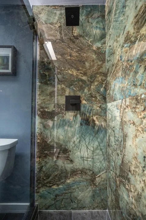 Walk-in shower lined floor to ceiling with green and bronze stone-look wall panels and a black shower valve