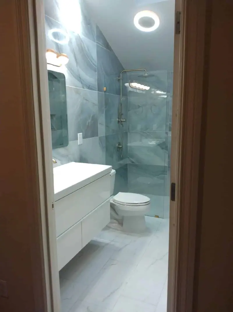 View through the doorway of a bathroom tiled in blue gray marble-look tile, with a floating white vanity, a toilet and a frameless glass shower