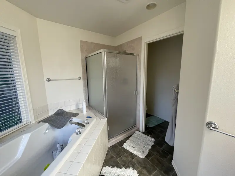 Old tub deck beside a framed corner shower stall with frosted glass, before the remodel
