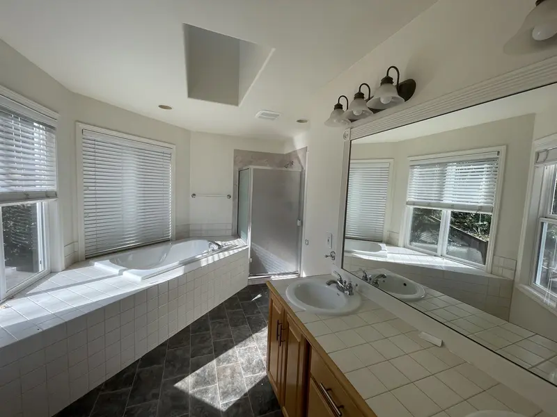 Tiled tub deck under three windows and an oak vanity with a tile counter, before the remodel