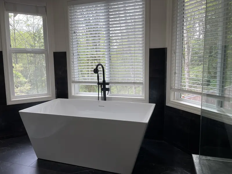 Angled view of the freestanding tub and dark wall tile under the bay windows