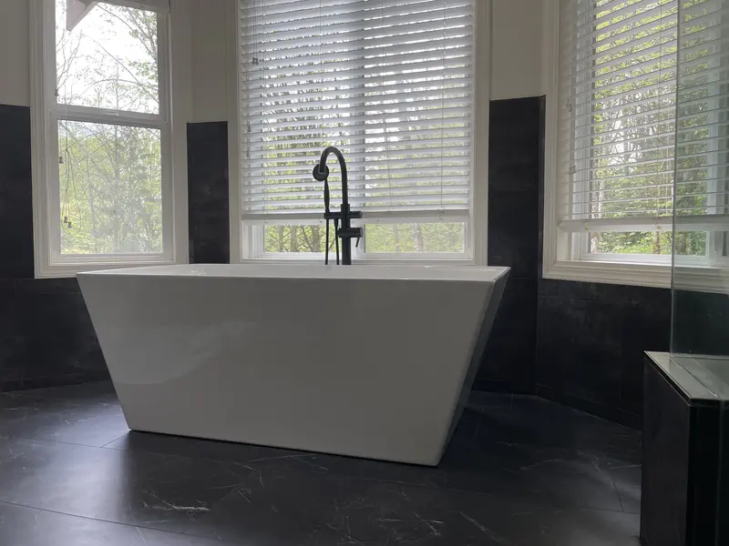 Freestanding tub set in a window bay with dark tile below the windows and a dark floor