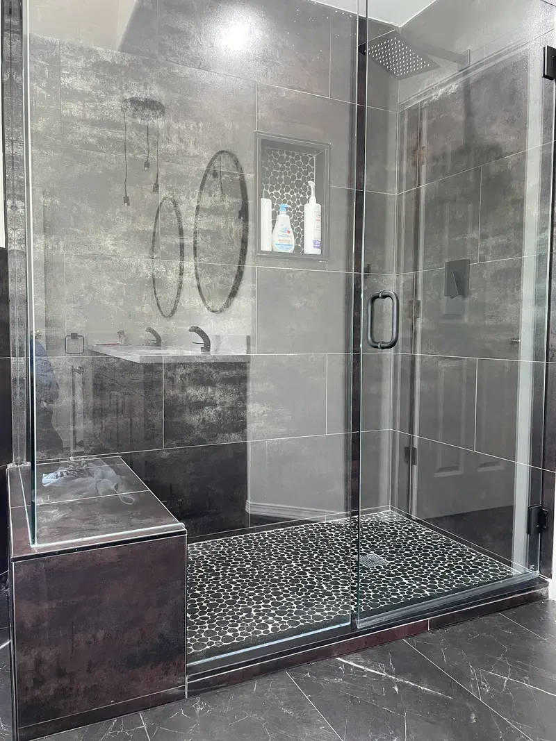 Frameless glass shower with a tiled bench, dark marble-look walls and a pebble floor