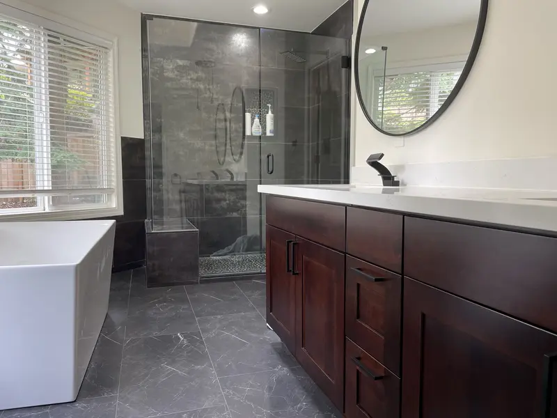 Tub, glass shower and espresso vanity with round black mirrors in one view