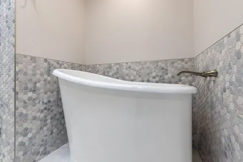 White freestanding soaking tub against a blue-gray hex mosaic wainscot with a wall-mounted filler