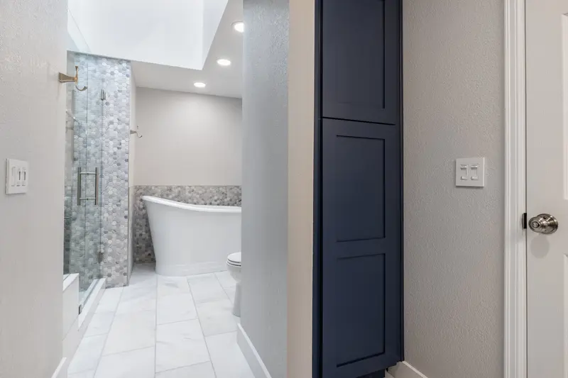 Tall navy linen cabinet beside the shower glass with the tub visible beyond