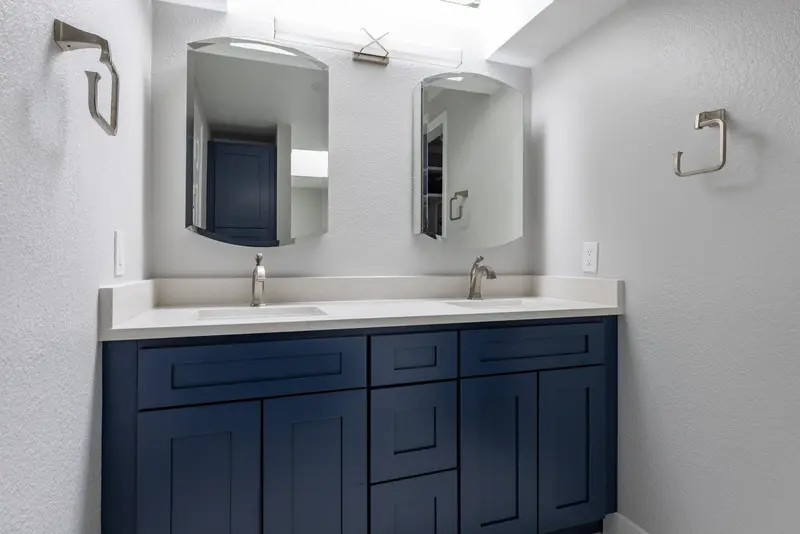 Navy vanity with white tops, two brushed faucets, rounded mirrors and towel rings