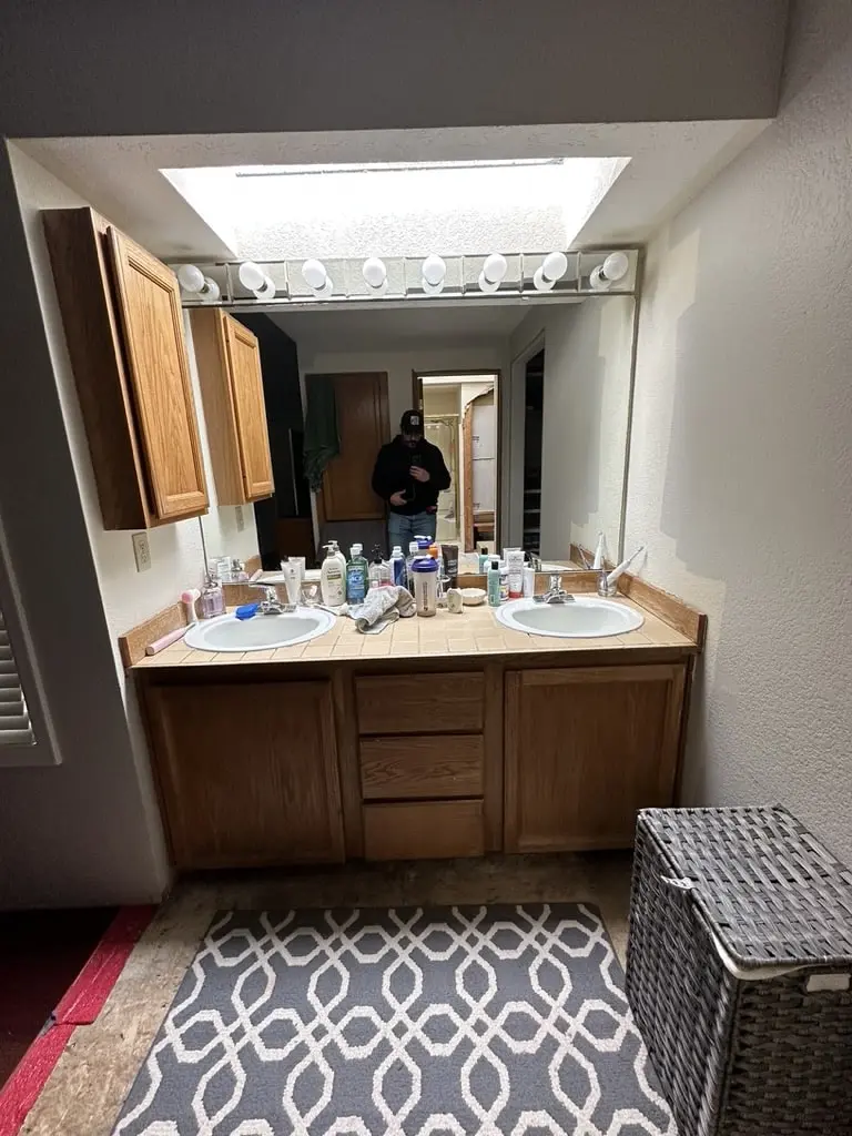 Master bathroom before the remodel with a wood double vanity, a light bar and a skylight above