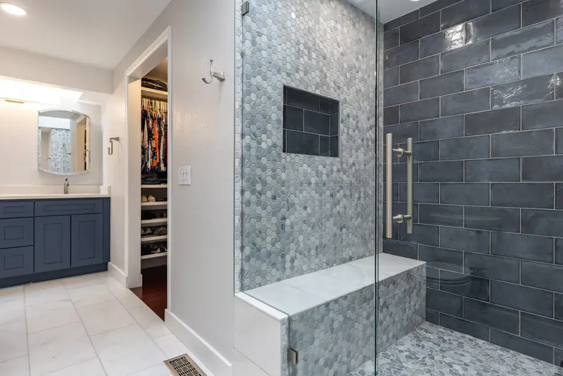 Shower with a bench and navy tile seen from the room, with the vanity and closet beyond