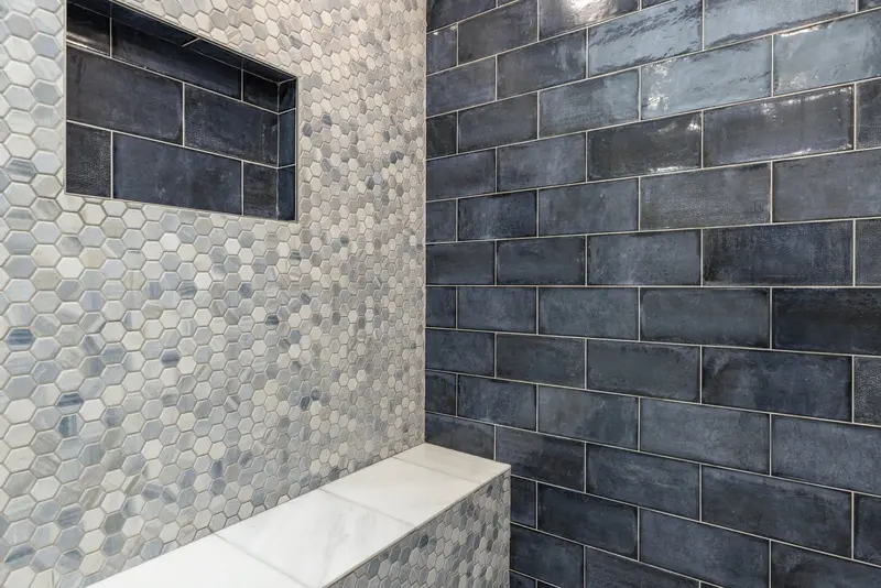Shower bench with a white top in front of a navy subway tile wall and a mosaic niche
