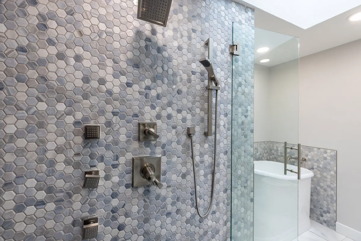 Blue-gray hex mosaic shower wall with a rain head, handheld, body sprays and brushed valves