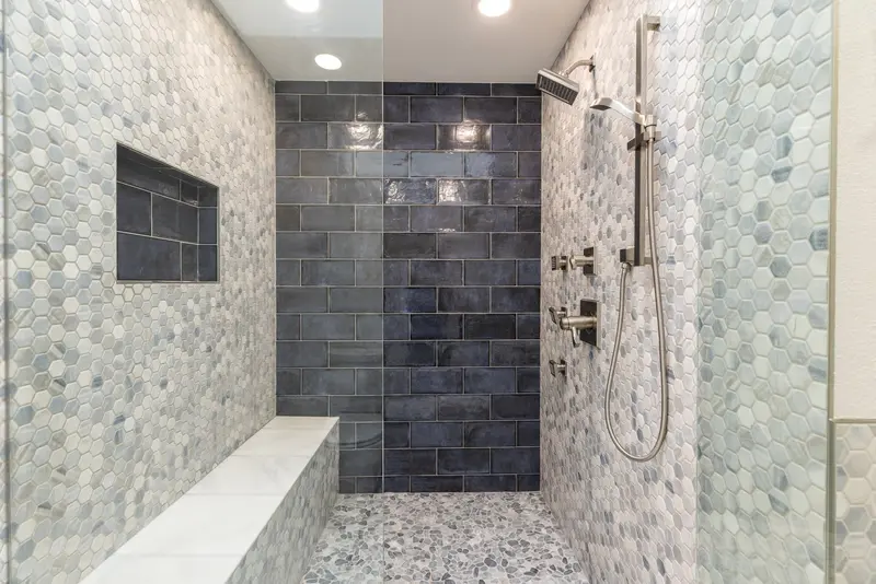 Walk-in shower with a navy subway tile back wall, mosaic side walls and a long niche